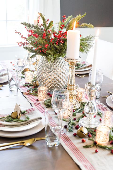 تزیین کریسمس میز ناهار خوری با گلدان و شاخ و برگ های سبز و میوه قرمز بری و شمع و شمعدان