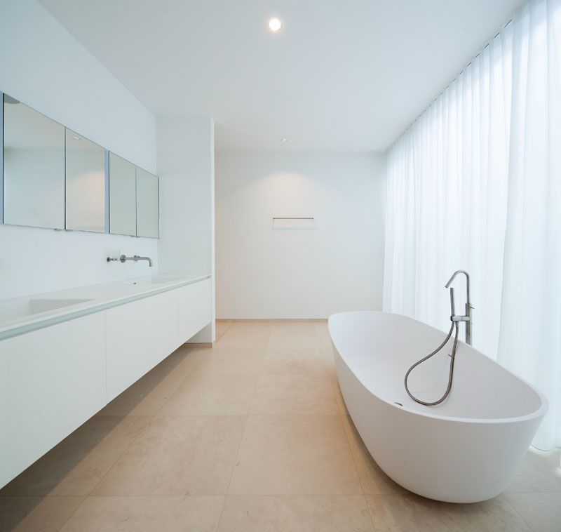 طراحی حمام مدرن و مینیمال بزرگ با رنگ سفید، وان جزیره ای و روشویی کابینت دار بدون پایه