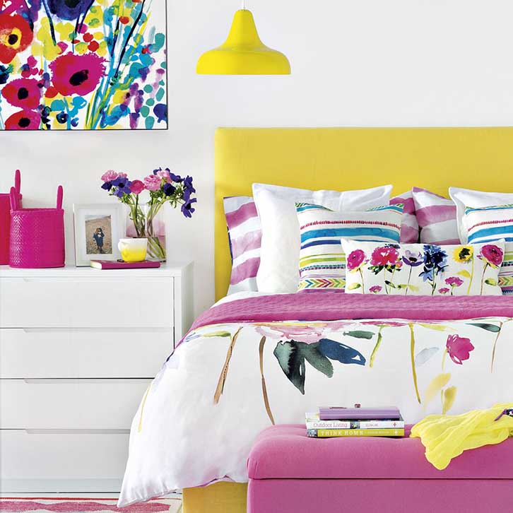 رنگ اتاق خواب سفید و زرد و صورتی و آبی با دیوارهای سفید و تخت زرد و روتختی صورتی آبی
