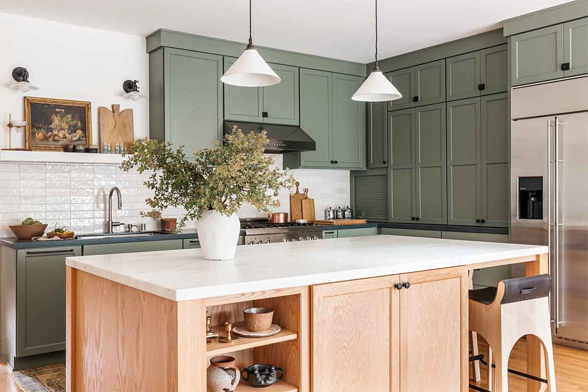 کابینت سبز تیره سیج با جزیره چوبی قهوه ای در آشپزخانه نئوکلاسیک با بین کابینتی آجری سفید