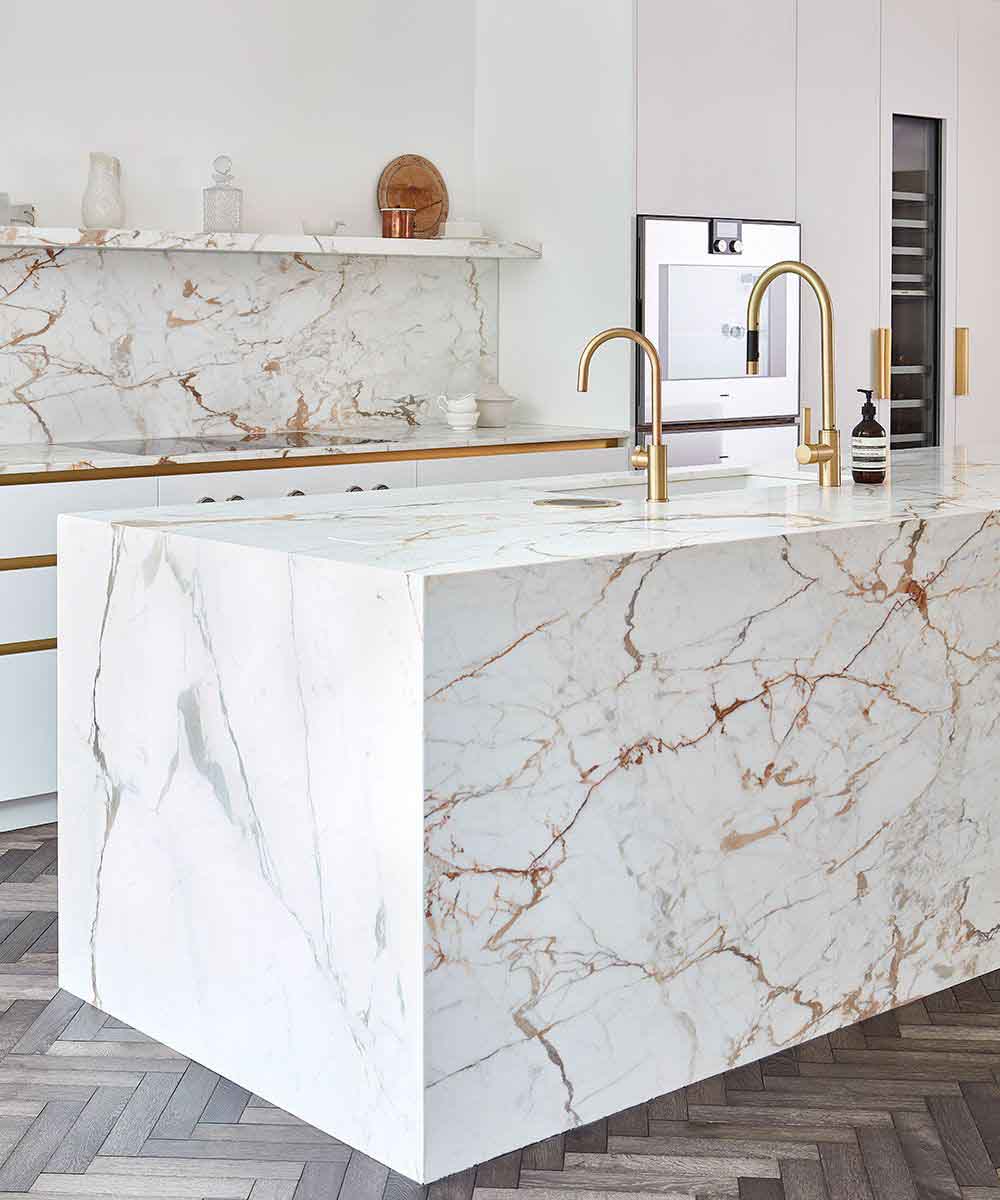 دکوراسیون سفید طلایی آشپزخانه مدرن با صفحه روی کابینت و بین کابینتی سنگ مرم سفید طلایی
